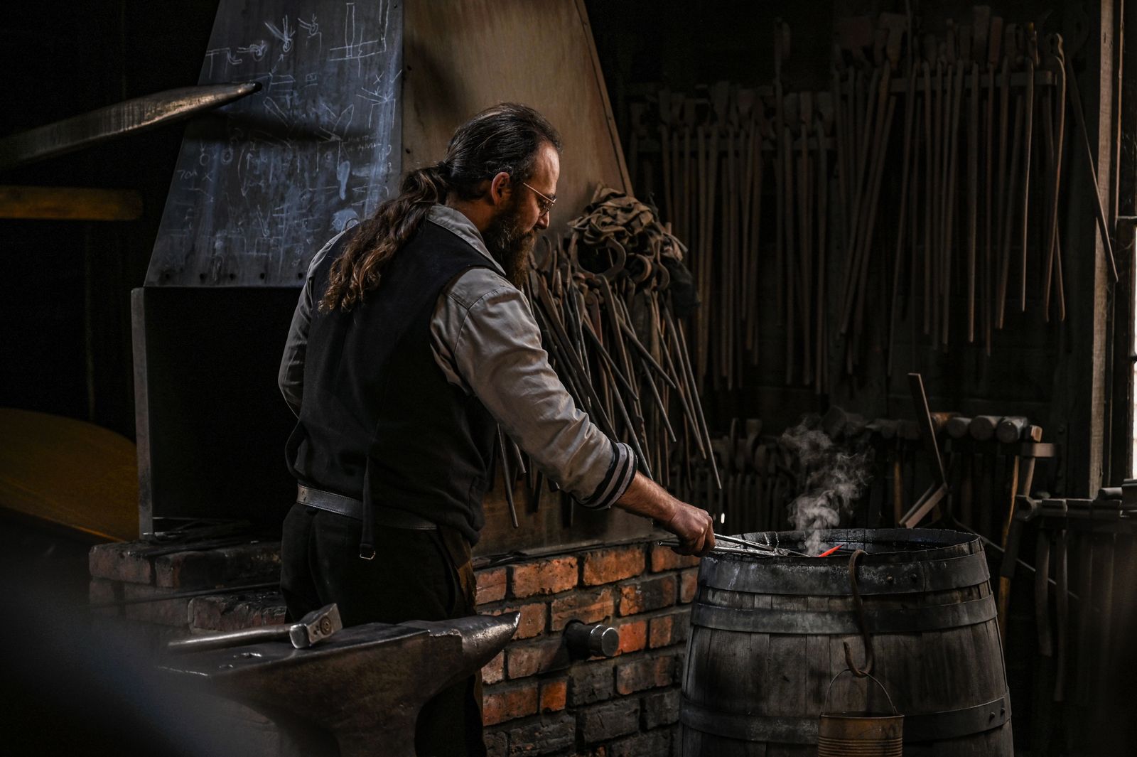 A blacksmith at work at an anvil in a forge, tools racked along the wall